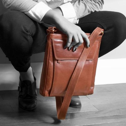 Stylish brown leather crossbody bag with a sleek design, held by a person.