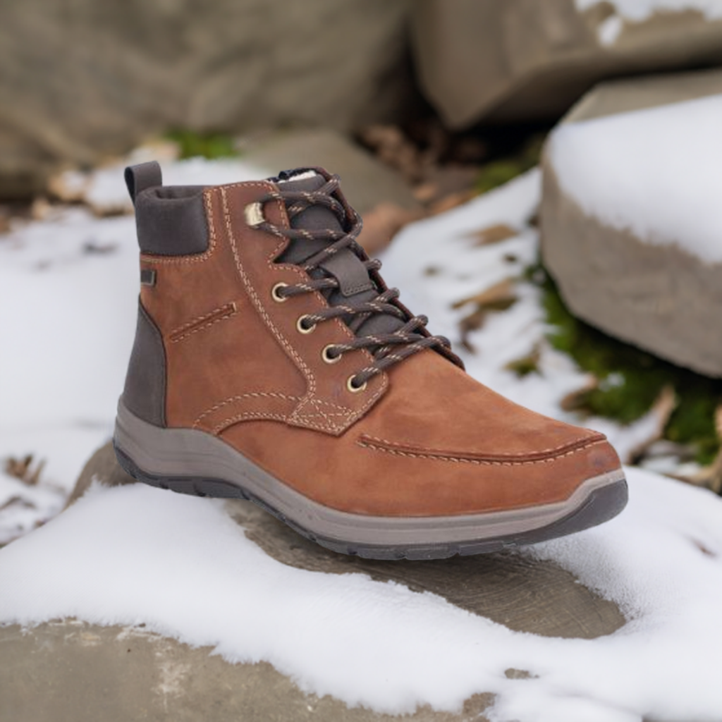 03610 Lace-Up Ankle Boot in brown leather with contrast dark trim, photographed on snowy surface. Features moc-toe design, rugged lacing system, and gray rubber sole. Water-repellent winter boot shown in outdoor setting with snow and moss accents.