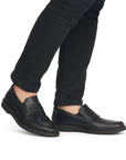 Men in in black jeans wearing black leather penny loafer dress shoe.