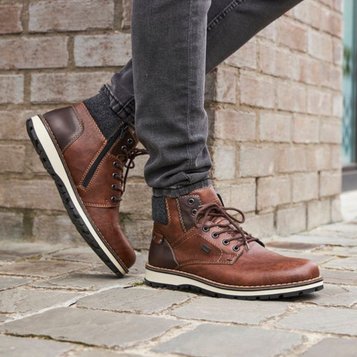 Legs in black jeans wearing brown ankle boot with textile cuff, laces, white midsole and brown outsole.