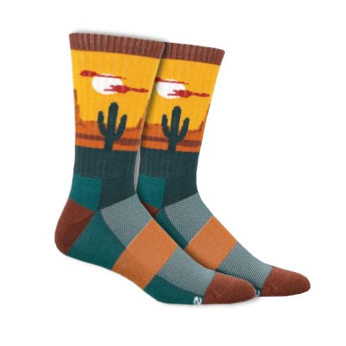 Wool socks with light blue, teal, and navy square pattern on foot, with geometric sunset image of desert around ankle cuff. Cuff, heel and toe are dark rust red color. There is an orange rectangle wrapping around the instep 