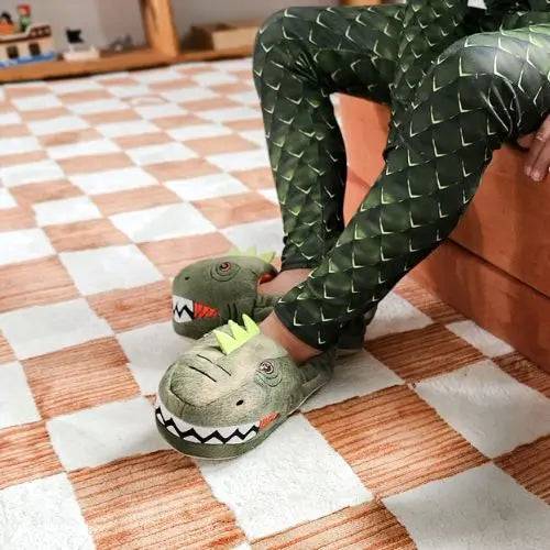 Person wearing dinosaur slippers and green scale-patterned pants sits on a bed on a checkered carpet.