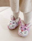 Child wearing pink and purple fluffy bunny slippers with adorable face design.