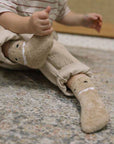 Toddler wearing beige dinosaur-themed cozy socks on a textured rug.