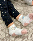 Toddler wearing white unicorn-themed cozy socks on a patterned rug.