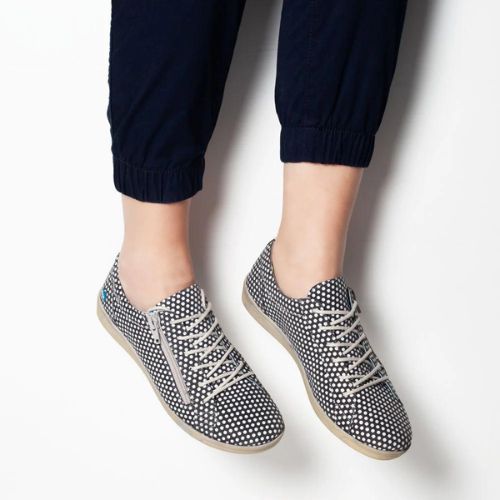 Woman sitting against a white backdrop wearing the Aika sneaker in polka. 