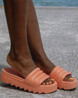 Woman on the street wearing the Pool Party Slide Sandals in Coral. She has matching colour painted toenails. 