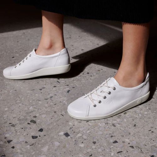 Woman taking a step onto pavement wearing the Ecco Soft 2.0 white Sneakers.