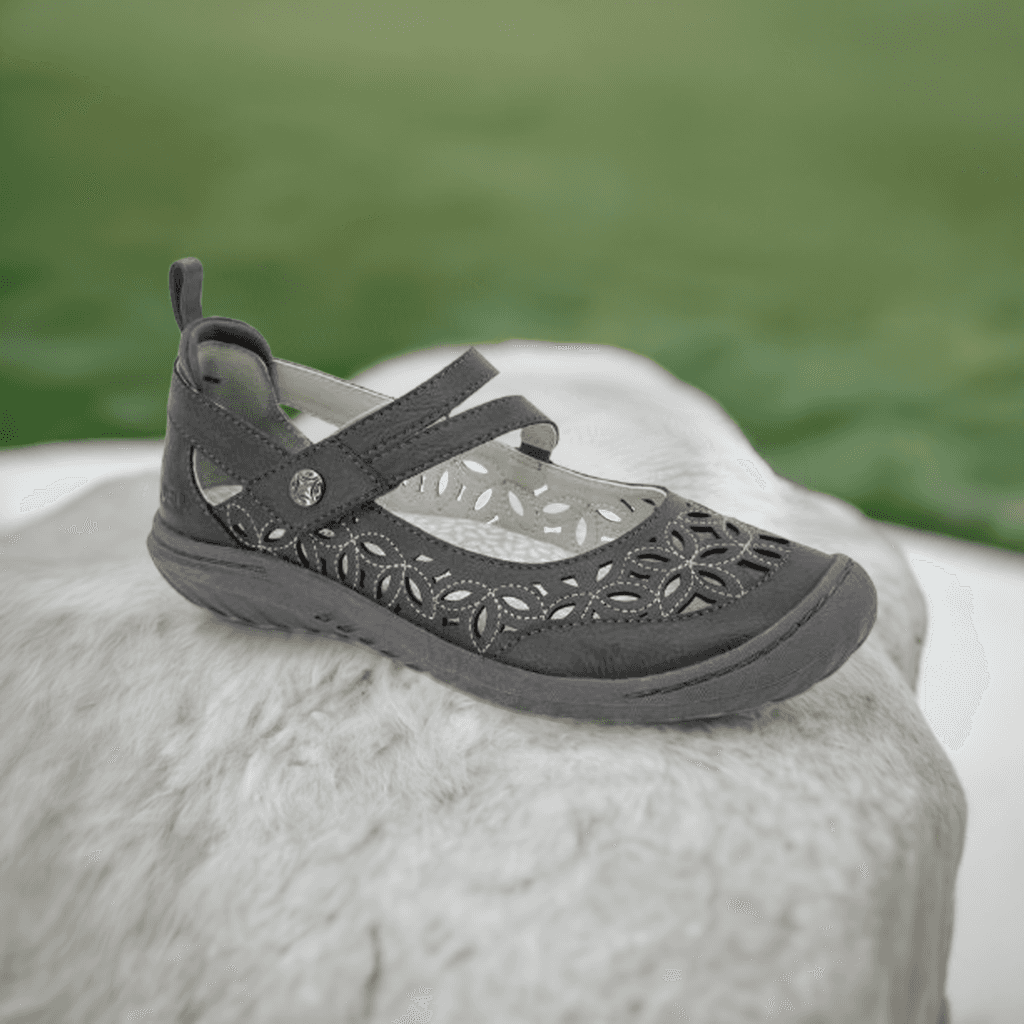 JBU Bellerose Encore Mary-Jane Flat in dark gray displayed outdoors on a rock, showcasing its floral perforations and rugged design.