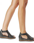 Person wearing black wedge sandal with floral cut-outs.