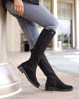 Legs in jeans wearing black tall boot with inside zipper and small silver Remonte emblem at top.