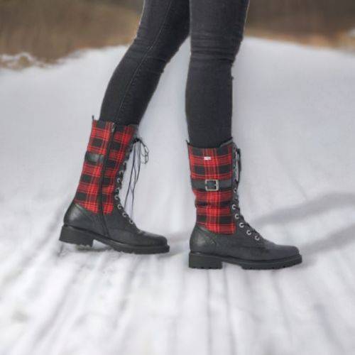 Model wearing black mid-calf boots with red plaid accents on a snowy path.