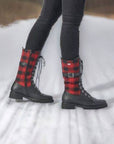 Model wearing black mid-calf boots with red plaid accents on a snowy path.