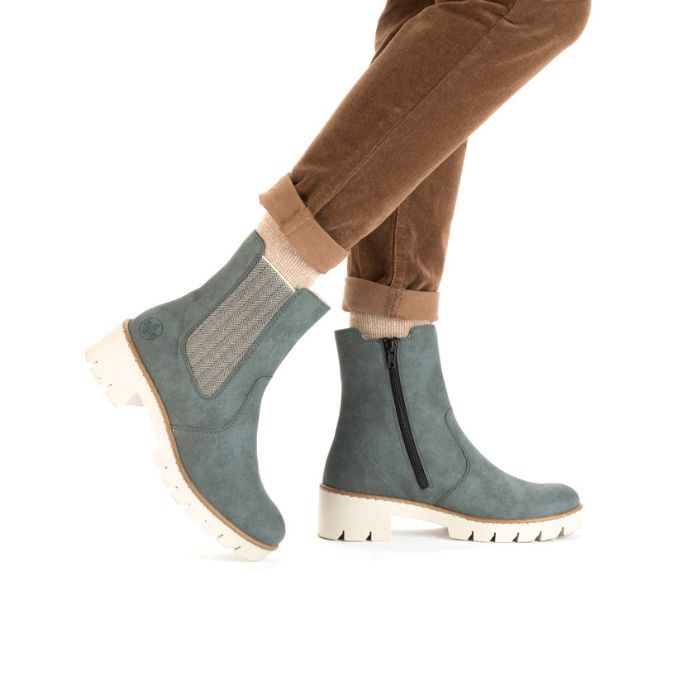 Women's legs in brown khaki pants wearing Rieker blue Chelsea boot with platform lugged white outsole.