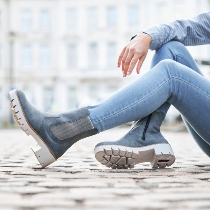 Women sitting on cobblestone in blue jeans wearing blue Chelsea boot with platform lugged white outsole.