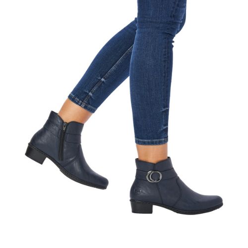 Woman in blue capri jeans wearing low stacked heel navy Rieker boots with circle buckle detail.