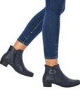 Woman in blue capri jeans wearing low stacked heel navy Rieker boots with circle buckle detail.