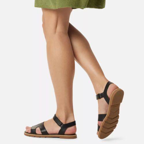 Person wearing Sorel Ella III Ankle Sandals with a green skirt, walking on a light background.