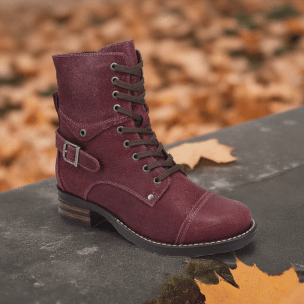 A Taos Crave Combat Boot with buckle detail lies on a stone with autumn leaves scattered around.