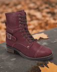 A Taos Crave Combat Boot with buckle detail lies on a stone with autumn leaves scattered around.