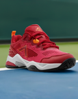 Red athletic shoe on sports court, featuring orange accents, a textured sole, and designed for lateral stability in pickleball.