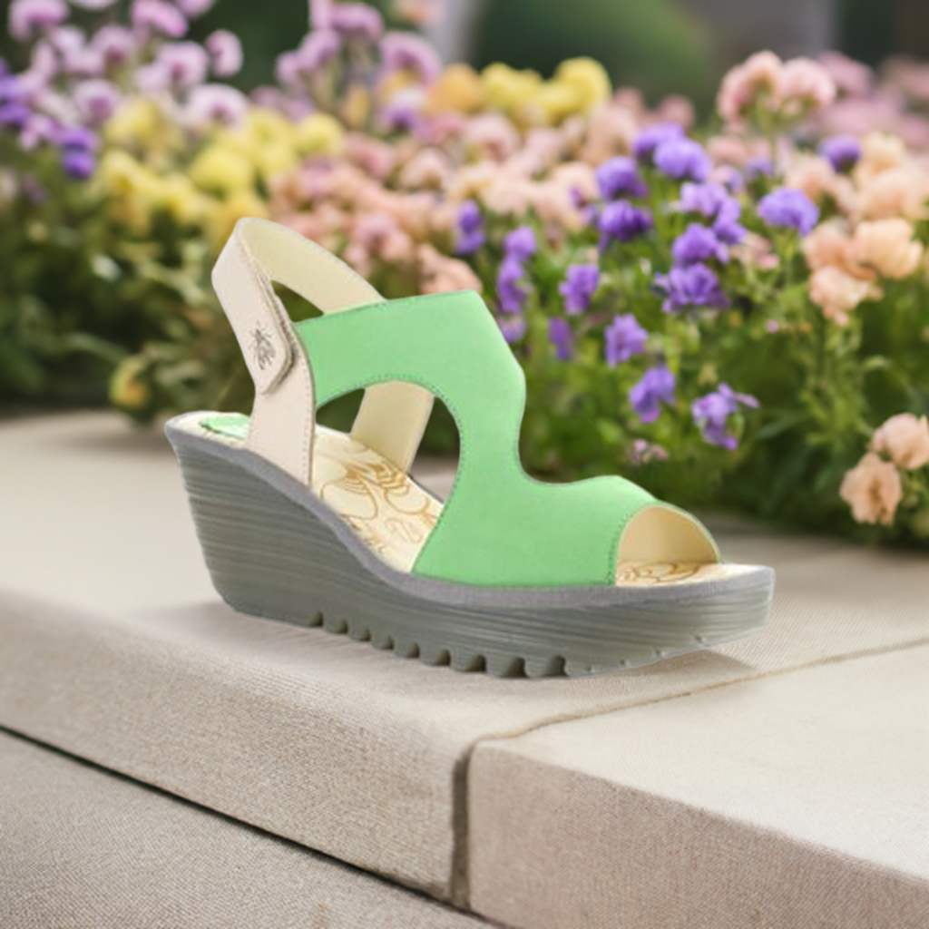 Yoxa Wedge Sandal in green displayed outdoors with floral background, highlighting its stylish design and comfort.