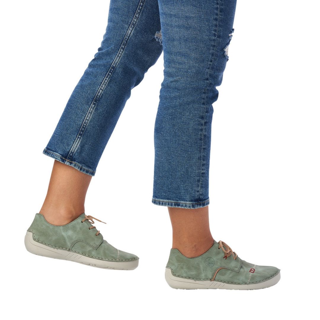 Person wearing jeans and mint Rieker lace-up sneakers.