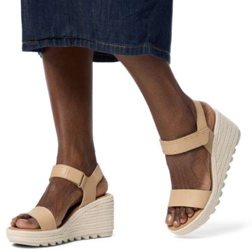 Person in a denim skirt wearing tan Sorels Cameron Wedge Sandal with adjustable ankle strap.