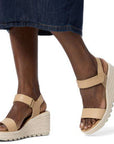 Person in a denim skirt wearing tan Sorels Cameron Wedge Sandal with adjustable ankle strap.