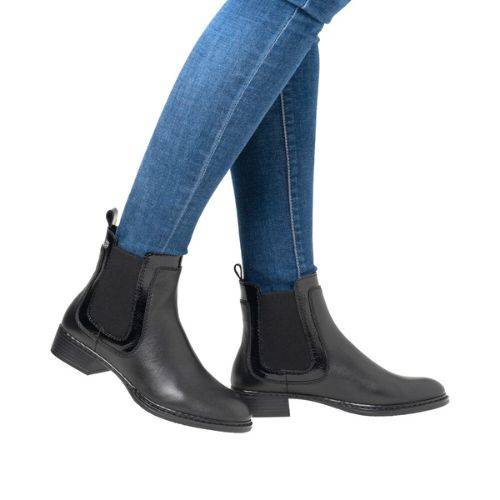 Person wearing genuine leather Chelsea boots and blue jeans on a white background.