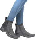 Person in black genuine leather ankle boots with shock absorbing outsole and blue jeans, side view.