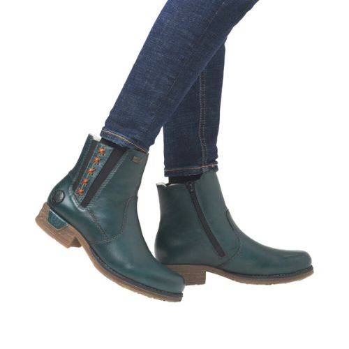 Person in jeans wearing teal ankle boots with black elastic goring red stitch details.