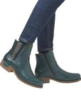 Person in jeans wearing teal ankle boots with black elastic goring red stitch details.