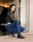 Women leaning against wall wearing black and bronze ankle boto with lace closure.