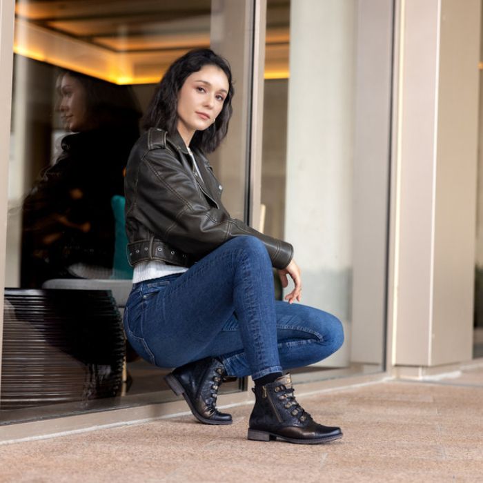 Women leaning against wall wearing black and bronze ankle boto with lace closure.