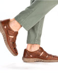 03578 Casual Fisherman Sandal shown in rich brown leather with adjustable Velcro closure, paired with sage green pants. Features breathable cutout design, comfortable rubber sole, and classic fisherman style construction for summer wear.