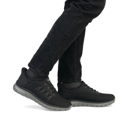 Person wearing Rieker B6656 slip-on sneakers in black, styled with black pants, highlighting casual comfort and versatility.