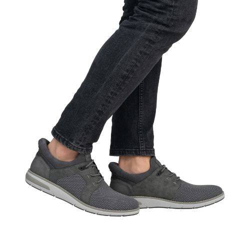 Man in black jeans wearing Rieker grey slip on lace sneakers.