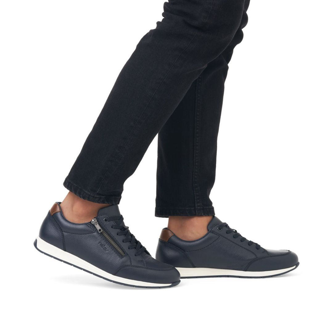 11903 Slip-On Lace Sneaker shown in navy blue with side zipper detail, white sole trim, and traditional lace-up design, displayed on feet wearing black jeans, highlighting its casual everyday style and convenient slip-on feature