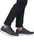 11903 Slip-On Lace Sneaker shown in navy blue with side zipper detail, white sole trim, and traditional lace-up design, displayed on feet wearing black jeans, highlighting its casual everyday style and convenient slip-on feature