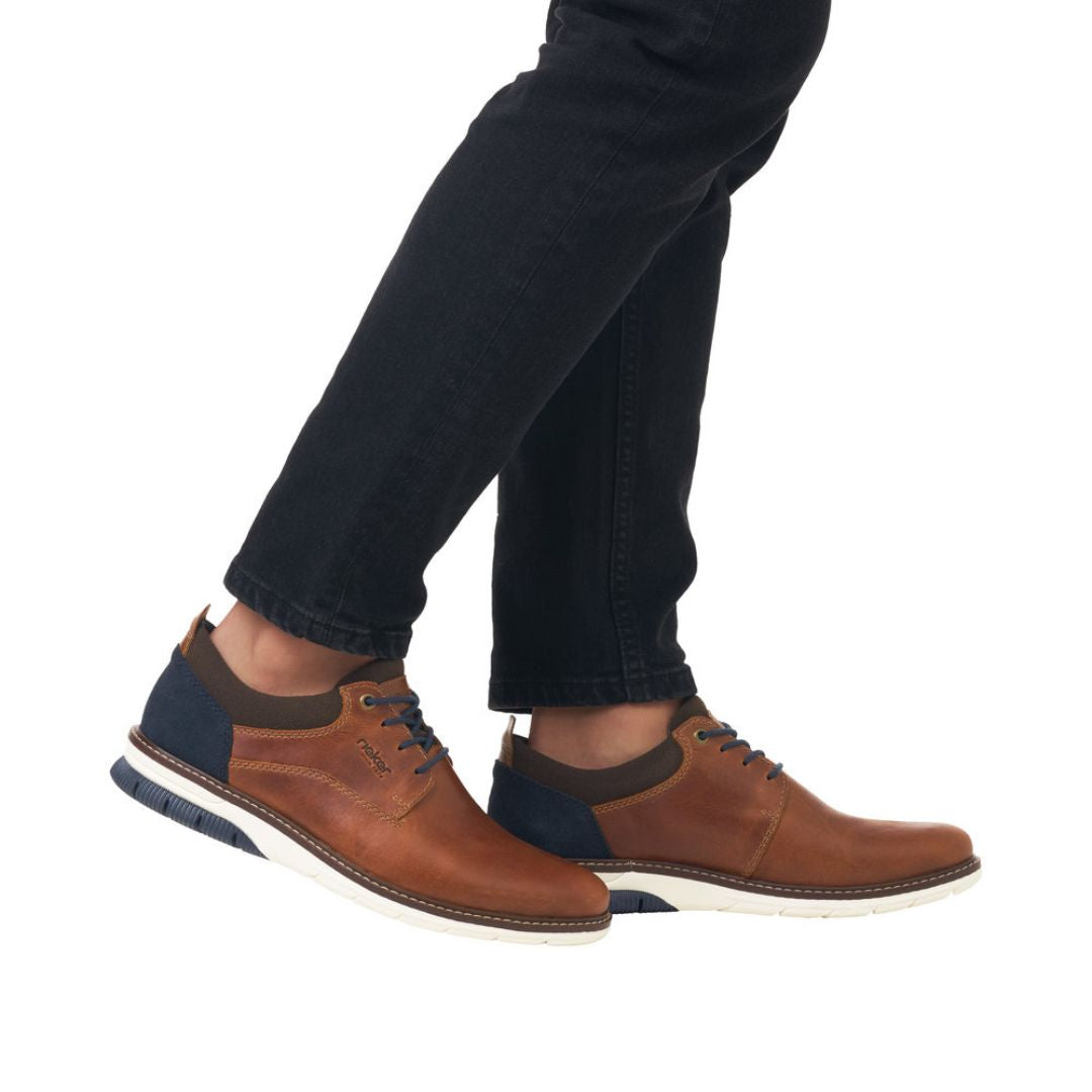 14405 Slip-On Lace Sneaker shown in brown leather with navy blue accents, featuring casual design with clean lines. White rubber outsole visible, sneaker displayed on foot wearing dark jeans, highlighting its everyday versatile style and comfortable fit.