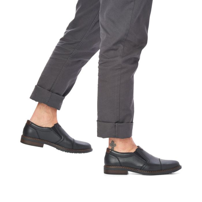 Legs in grey cuffed pants wearing black leather slip on shoe with toe cap.