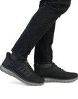 Person wearing Rieker B6656 slip-on sneakers in black, styled with black pants, highlighting casual comfort and versatility.