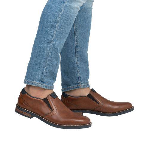 Man in blue jeans with brown leather semi-dress loafers with Rieker logo on tongue. 