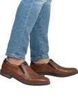 Man in blue jeans with brown leather semi-dress loafers with Rieker logo on tongue. 