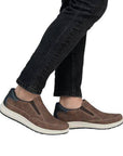 Man in black jeans wearing Rieker brown leather perforated slip on sneakers.