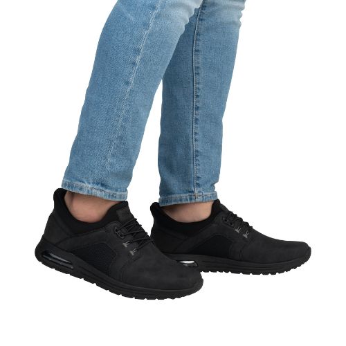 Legs of man in blue jeans wearing black manmade leather sneakers.