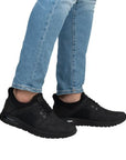 Legs of man in blue jeans wearing black manmade leather sneakers.