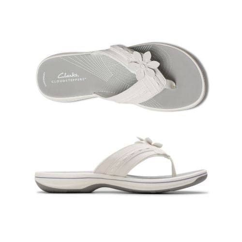 Profile and top view of White thong sandal with white midsole, grey footbed with white designs including Clarks Cloudsteppers logo, fabric toe post, and adjustable white strap with white flower. Dark grey outsole with rocker bottom design.