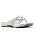 White thong sandal with white midsole, grey footbed with white designs including Clarks Cloudsteppers logo, fabric toe post, and adjustable white strap with white flower. Dark grey outsole with rocker bottom design.